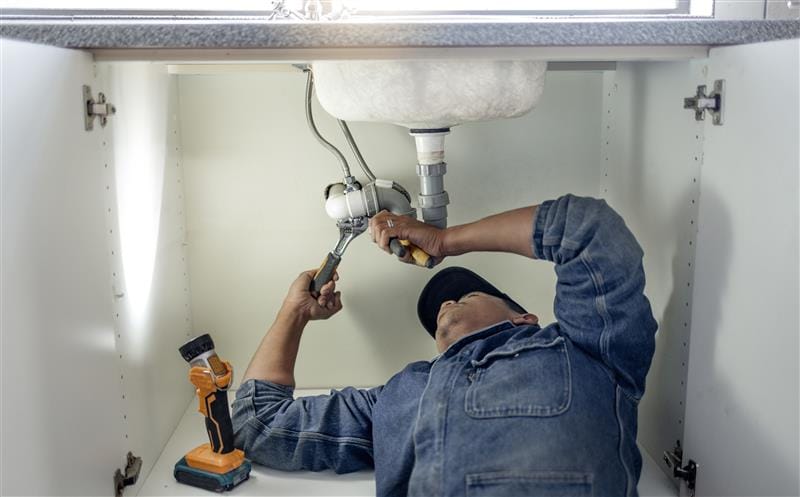 Plumber repairing pipes beneath a bathroom sink in Ormond Beach