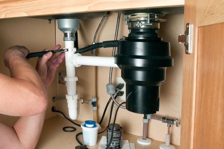 Plumber installing a garbage disposal beneath a kitchen sink in Ormond Beach