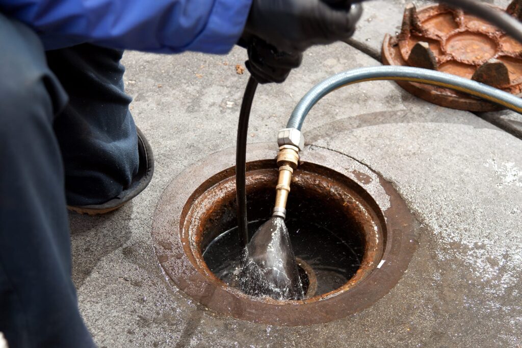 Plumber hydro jetting a sewer line through a manhole in Ormond Beach