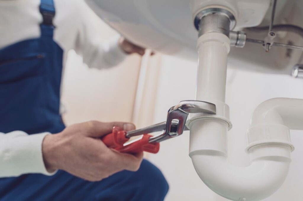 Plumber repairing a white drain pipe beneath a sink in Ormond Beach