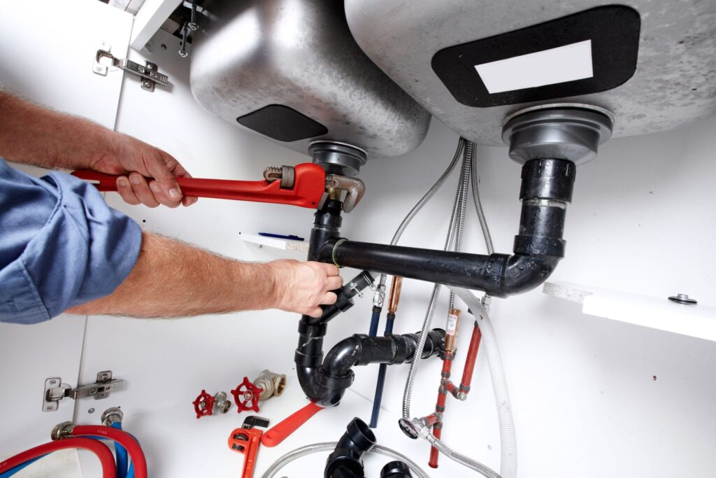 Plumber repairing drain pipes beneath a kitchen sink in Ormond Beach